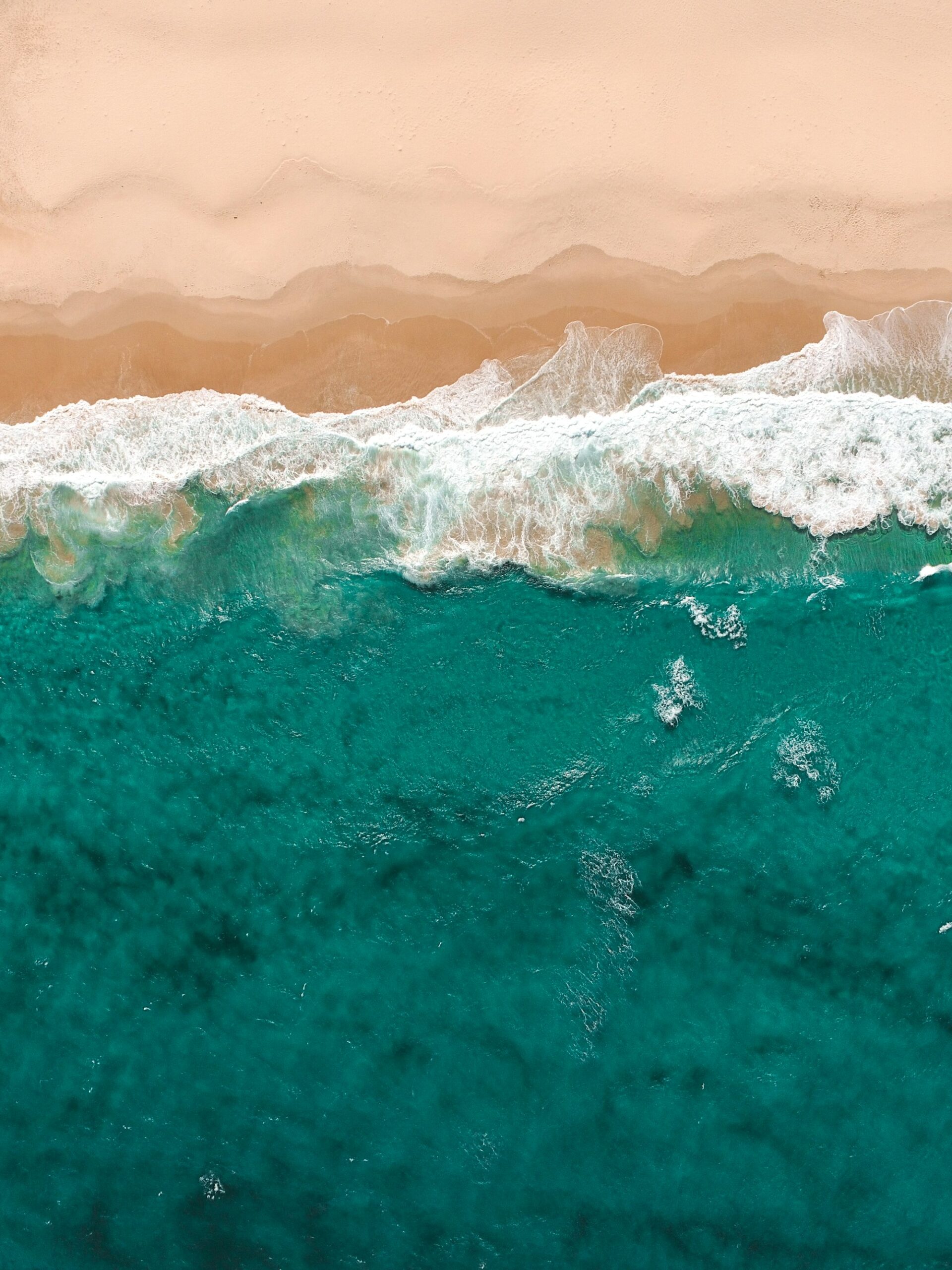 Aerial view of turquoise waves rolling onto golden sand